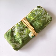 a green and white flowered pouch with a wooden tie on the front, sitting on a white surface