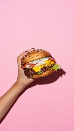 a hand holding up a hamburger on a pink background