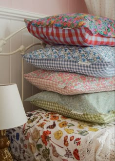 a stack of pillows sitting on top of a bed next to a night stand with a lamp