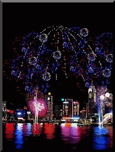 fireworks are lit up in the night sky over a body of water with city lights