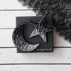 a star and moon brooch sitting on top of a piece of black fabric next to a lace doily