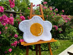 an egg shell is on top of a wooden easel in front of pink flowers