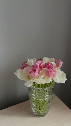 a vase filled with pink and white flowers on top of a wooden table next to a gray wall