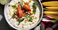 a white bowl filled with hummus, carrots and celery next to sliced radishes