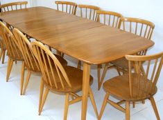 a wooden table with six chairs around it and a white wall in the back ground