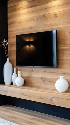 Modern interior with light oak floating TV stand holding flat-screen TV on black wall, white vases. Floating Tv Stand Diy, Under Mounted Tv, Minimalist Tv Unit, Tv Stand Inspiration, Tv Console Diy, Tv Stand Diy, Floating Tv Stands, Floating Tv Console, Wood Entertainment Center