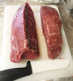 two pieces of raw meat sitting on top of a cutting board next to a knife