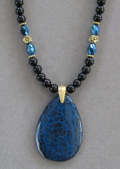 NOTE: Fire Agates are natural volcanic stone and they are not perfect due to the nature of the stone. However, they are very pretty! The pendant is unusual and it is thicker than most because it comes from volcanic rock. This is a lovely teardrop shaped Black and Blue Fire Agate Pendant Necklace.   The beads in the necklace are genuine black agate with blue crystal beads that pick up the colors of the pendant with silver crystal accents.   The pendant is polished. The pendant measures 2 inches long x 1 1/2 inches wide.  This is a unique one of a kind necklace.  It's 16 inches long and adjustable to 20.  All my jewelry is unique and one of a kind. Similar quality jewelry is priced at double. I source the stone pendants from all over the world. All pendants and necklaces are made with semipr Bead Threading, Jewellery Patterns, Wooden Bead Jewelry, Jewelry 2024, Blue Crystal Beads, Beaded Designs, Diy Necklaces, Agate Pendant Necklace, Dragon Vein Agate