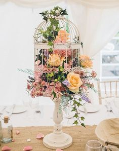 a birdcage filled with flowers sitting on top of a table next to plates