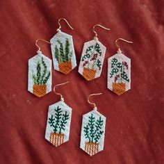 four cross stitch earrings with cactus designs on them sitting on a red cloth covered surface