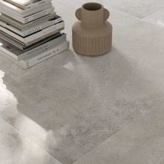 a stack of books sitting next to a vase on top of a white tile floor