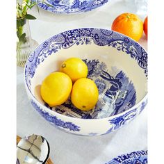 three lemons in a blue and white bowl on top of a table with plates