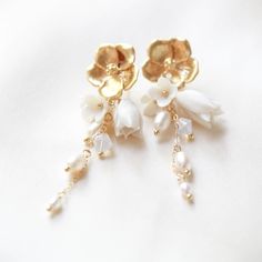 two pairs of earrings with flowers and pearls hanging from the earwires on a white surface