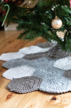 a christmas tree is decorated with ornaments and knitted rugs in shades of gray, white and grey