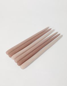 four candles are lined up on a white surface, one is pink and the other is beige