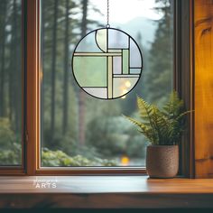 a potted plant sitting next to a window sill with a circular stained glass hanging from it