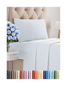 a bed with blue and white striped sheets next to a vase filled with flowers on top of it