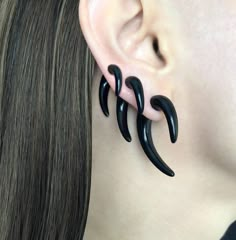 a woman wearing black earrings with three long, curved horns on her ear and the end of