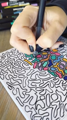 a person drawing on a piece of paper with a black marker and colored pencils