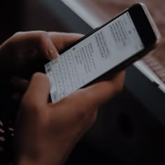 a person holding a cell phone in their hand and typing on the screen while sitting at a table