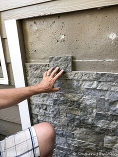 a man sitting on the ground next to a brick wall with his hand reaching for something