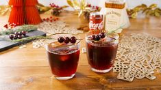 two glasses filled with liquid sitting on top of a wooden table next to christmas decorations