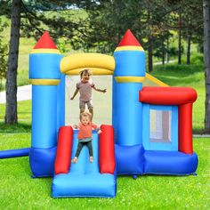 two children jumping on a bouncy castle in the grass with trees in the background