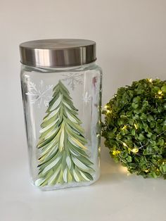 a glass jar with a christmas tree painted on it next to a potted plant