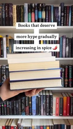 a person holding up a stack of books in front of a book shelf filled with books