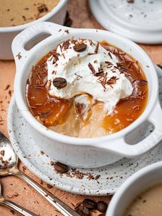 a bowl filled with pudding and whipped cream on top of a wooden table next to spoons