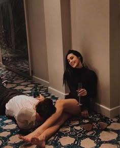 two people are sitting on the floor and one person is holding a wine glass in her hand