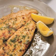 two pieces of fish are on a plate with lemon wedges and parmesan cheese