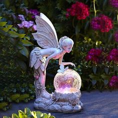 a fairy figurine sitting on top of a rock in front of some flowers