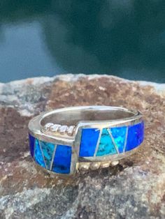 This beautifully well crafted Band ring has been handmade by a Navajo Artisan. The Colors of the Ring come from Lapis Lazuli, Turquoise and Blue Opal. The ring is a size 5.5 and the face is 3/4 long and 1/4 wide. The designs on the rings are a bit different due to nature of the natural stones. Winds of Wisdom (Lapis Lazuli, Turquoise and Blue Opal. The Navajo (Dine) believe that the wind is a powerful source. The native tradition believes that at any moment, the blowing wind can inspire one with Handmade Southwestern Style Open Ring, Unique Turquoise Opal Ring For Anniversary, Artisan Turquoise Ring Stamped 925, Artisan Turquoise Ring, Adjustable Blue Jewelry With Accent Stones, Blue Artisan Jewelry For Anniversary, Southwestern Handmade Open Ring, Artisan Blue Turquoise Ring Stamped 925, Southwestern Blue Jewelry For Anniversary