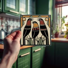 a hand holding up a card with two birds on it in a green kitchen area