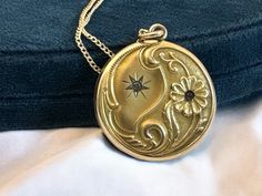 Description: Lovely antique Art Nouveau gold filled photo locket on a 14K gold filled chain. The front features an ornate repousse design with flowers and some leafy and curling designs on the bottom edge and two round faceted paste (glass) gems. The locket hangs on a new 14K gold filled curb chain with a spring ring clasp.  On the locket front top left section is an etched starburst shape that has a clear paste gem set inside it. On the right bottom side is a raised ten-petaled flower with a wonderful Repousse curled stem. The flower is set with a pink paste gem in the center. The flower and its stem along with some other decorative swirls fill up and curl around the bottom of the locket and create a lovely contrast to the starburst on a satin background on the opposite / top left side. Satin Background, Antique Locket, Pink Foil, Glass Gems, Photo Locket, Locket Necklace, Gold Filled Chain, Curb Chain, Antique Items