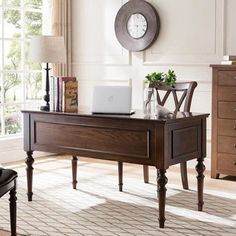 a wooden desk with a laptop on it in front of a window and a clock mounted to the wall