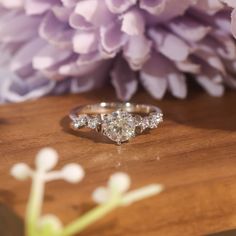 a diamond engagement ring sitting on top of a wooden table next to purple and white flowers