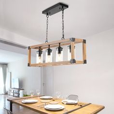 a wooden table with plates and glasses on it in front of a light fixture hanging from the ceiling