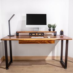 a wooden desk with a computer monitor and keyboard on it, in front of a white wall