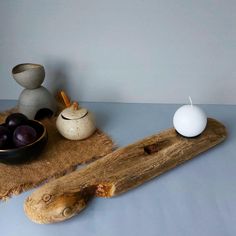 a wooden table topped with two vases next to a bowl filled with plums