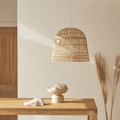 a wooden table topped with a white bowl next to a light hanging from a ceiling fixture