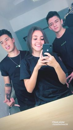 two men and a woman taking a selfie in front of a mirror with their cell phone