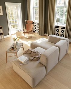 a living room filled with furniture next to two large windows in front of a wooden floor