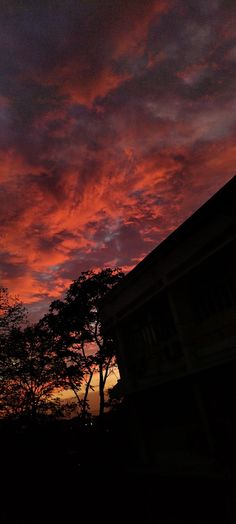 the sky is red and purple as the sun sets in the distance behind some trees