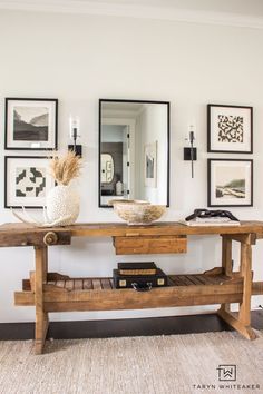 a wooden bench sitting under a mirror in a living room next to pictures on the wall