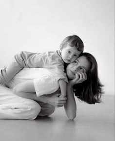 a woman holding a child while laying on the floor in front of a white wall