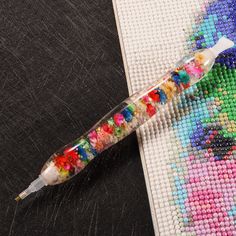 a needle - point pen is sitting on a piece of fabric next to some beads