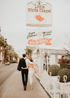 a man and woman walking down the sidewalk in front of a white chapel