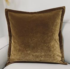 a brown velvet pillow sitting on top of a white couch next to a vase with flowers